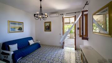 Una habitación con un sofá azul, una araña de techo, dos cuadros enmarcados, una escalera y un ventanal con vistas.