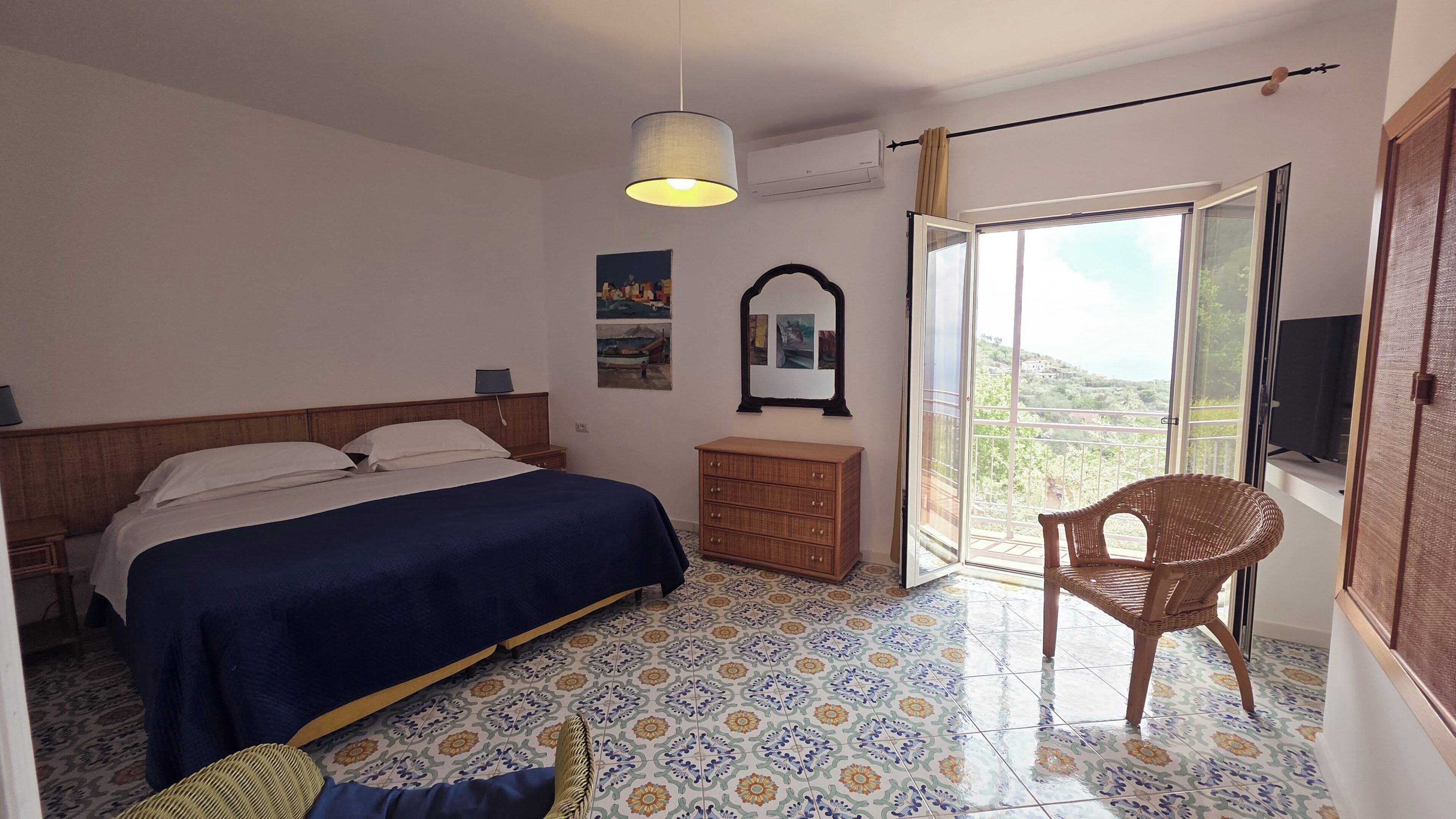 A bedroom with a bed, a dresser, a chair, a hanging lamp, a mirror, and a window with a view.
