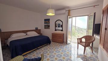 Ein Schlafzimmer mit Bett, Schminktisch, Sessel, Hängeleuchte, Spiegel und einem Fenster mit Aussicht.
