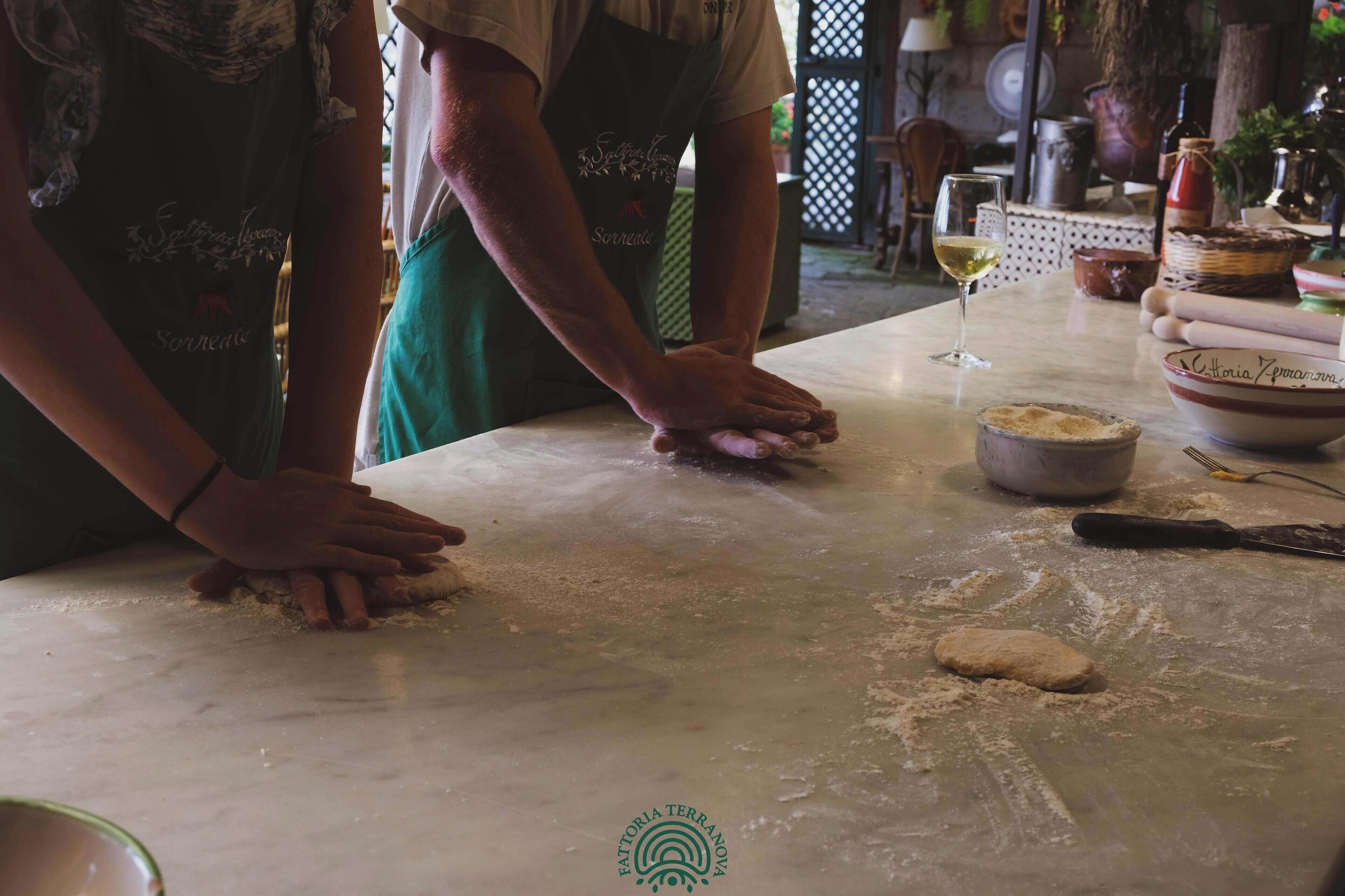 Two people kneading dough on a marble countertop in a kitchen setting.