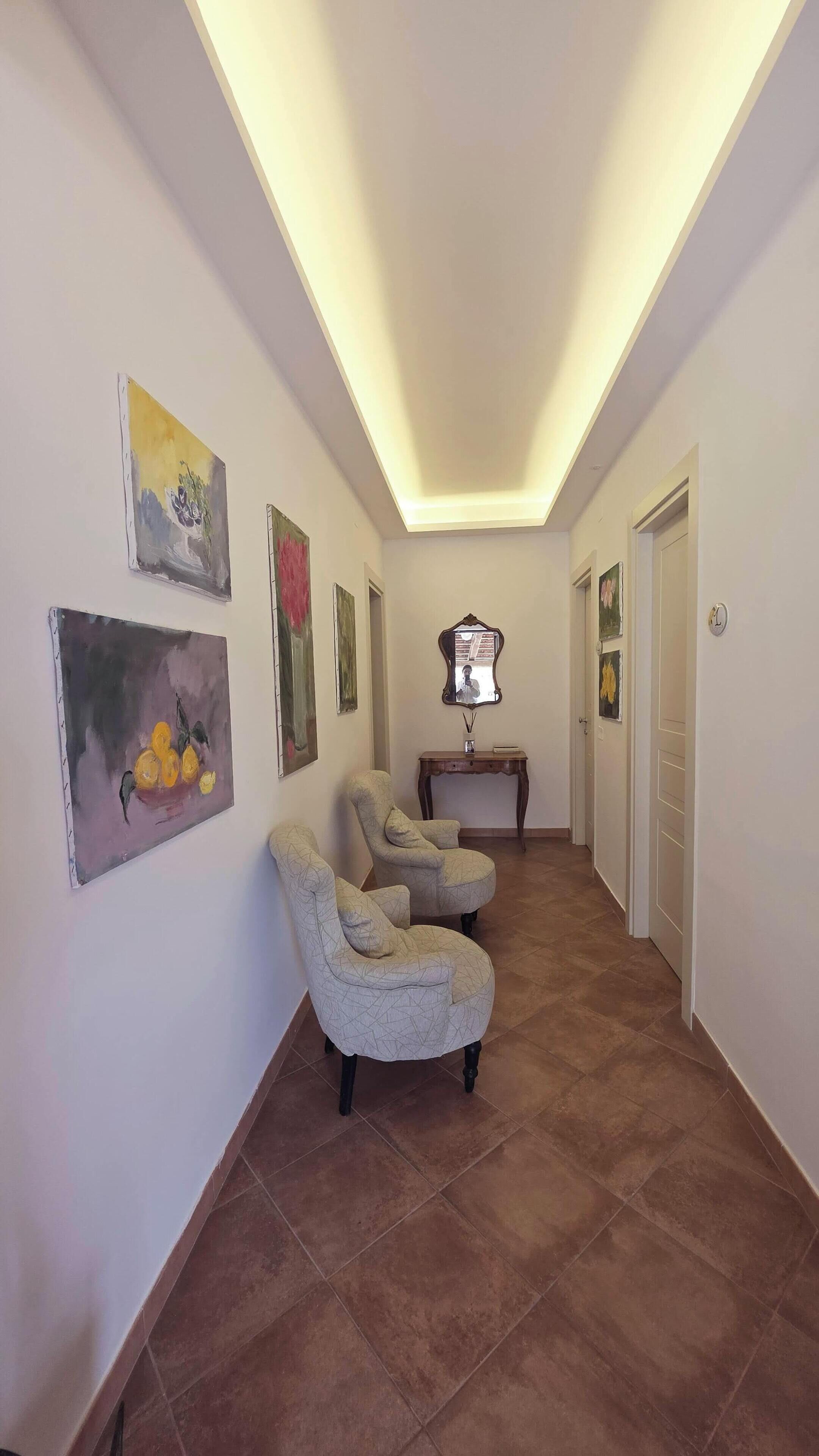 A hallway with two armchairs, a mirror, and artwork on the walls.