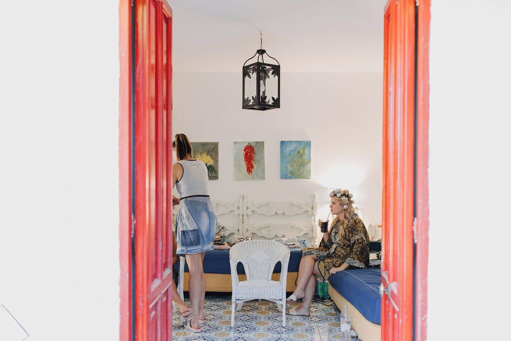 A room with a bed, a white chair, and a table with a lamp.