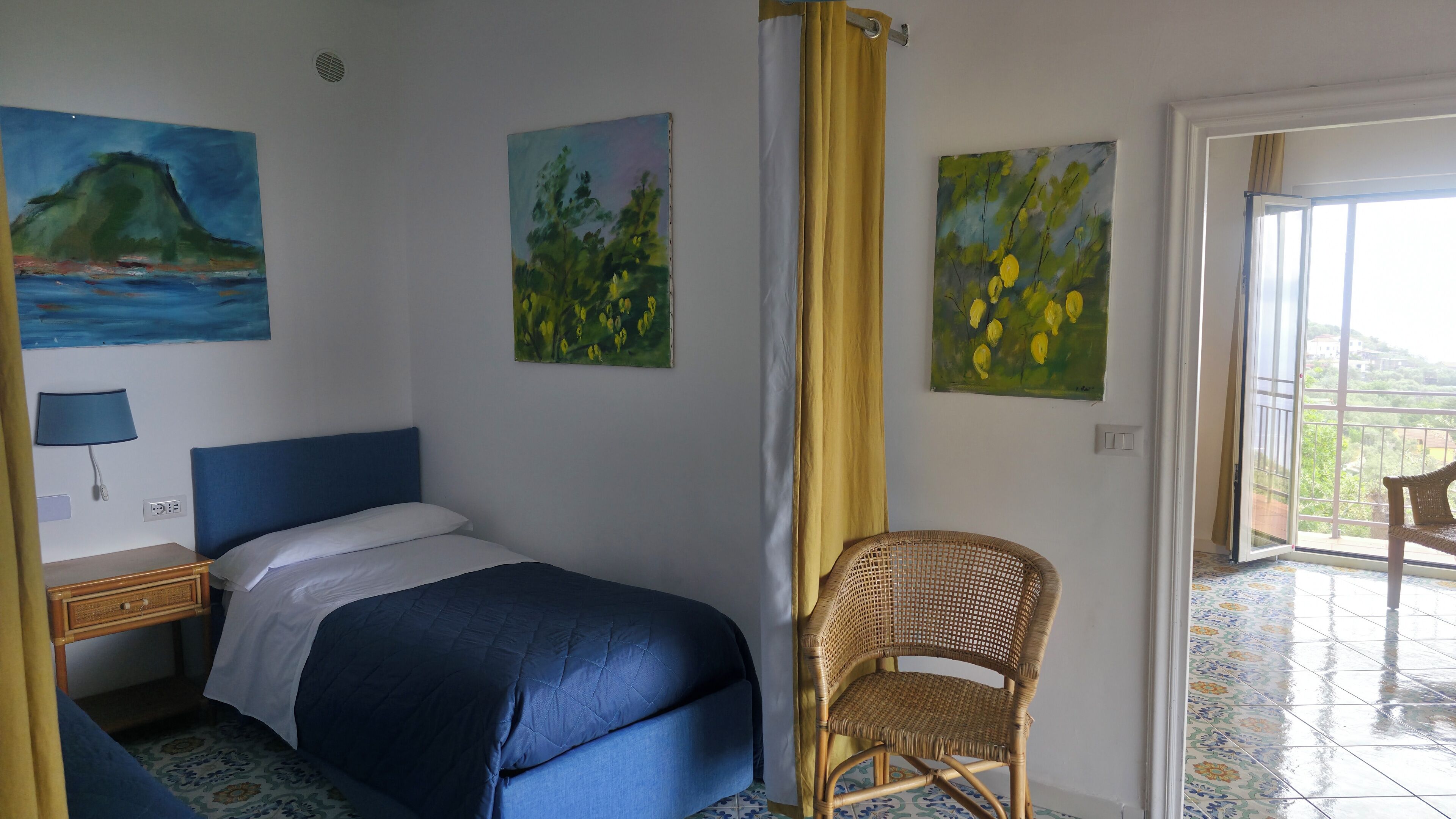 A hotel room with a bed, a chair, and three paintings on the wall.