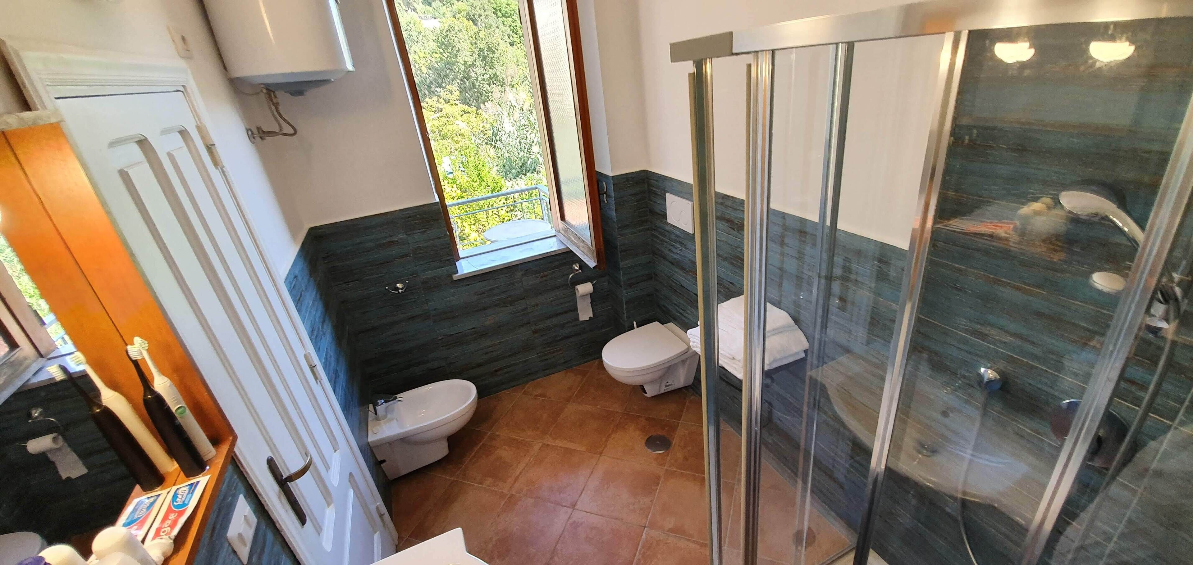 A modern bathroom with a glass shower enclosure, a toilet, and a bidet.