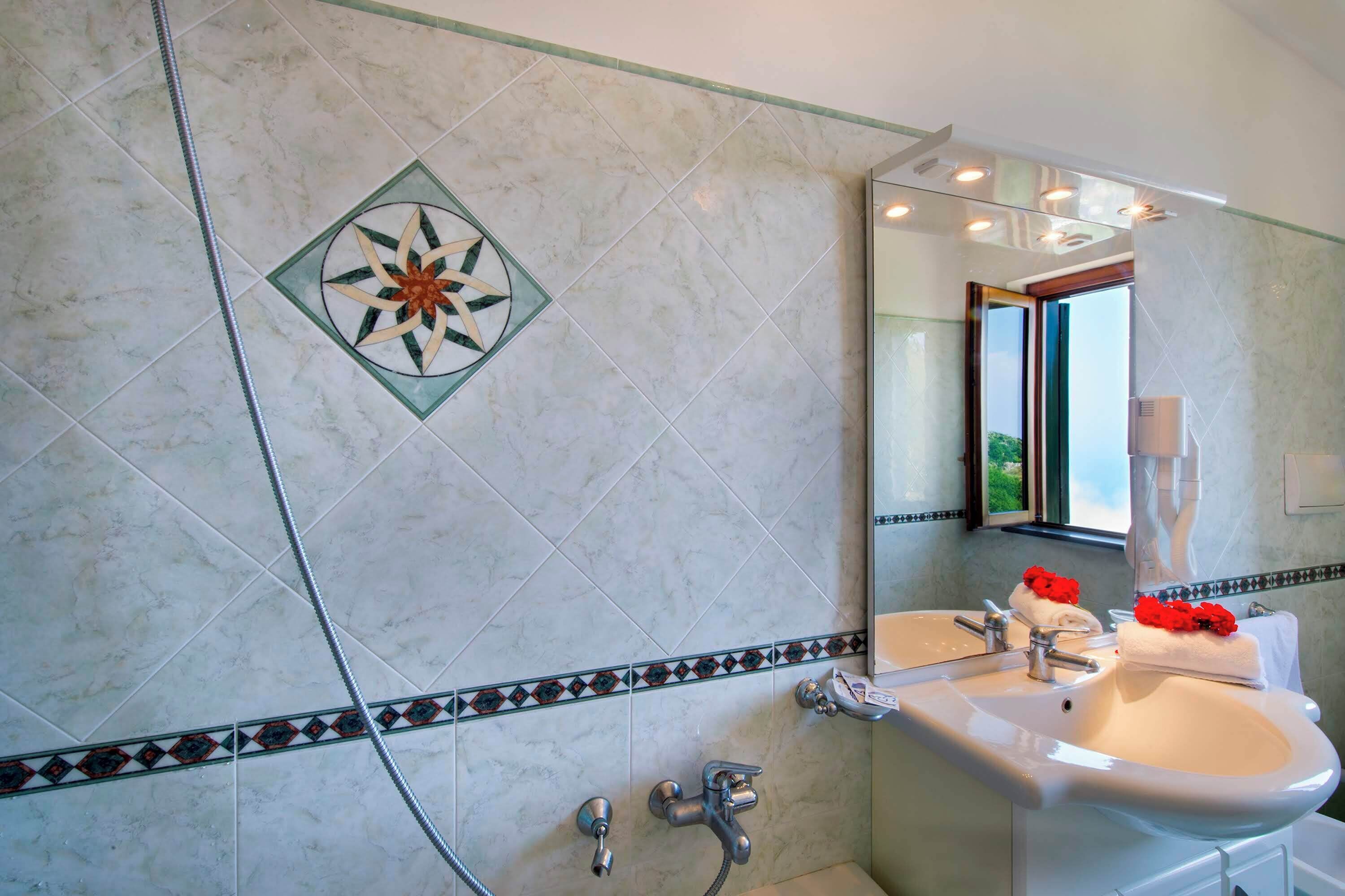 Een badkamer met een grote spiegel, twee wasbakken, een douche en decoratieve tegels.