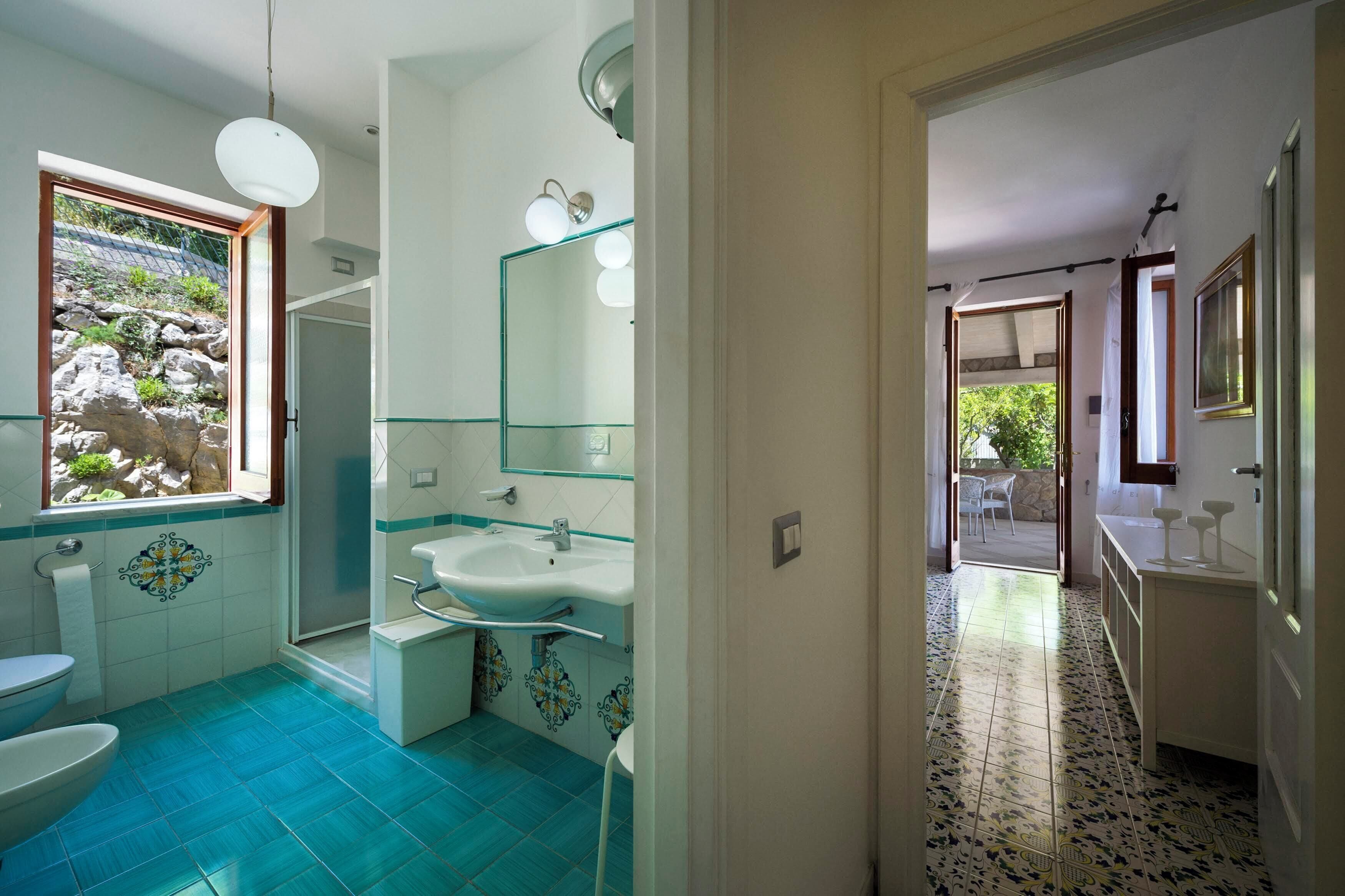Une salle de bain avec un sol carrelé de carreaux bleus, un lavabo blanc, une cabine de douche en verre et un grand miroir.