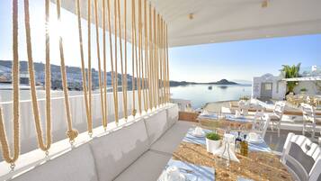 Una terraza con una mesa lista para comer, con vistas al mar tranquilo y a un pueblo costero.