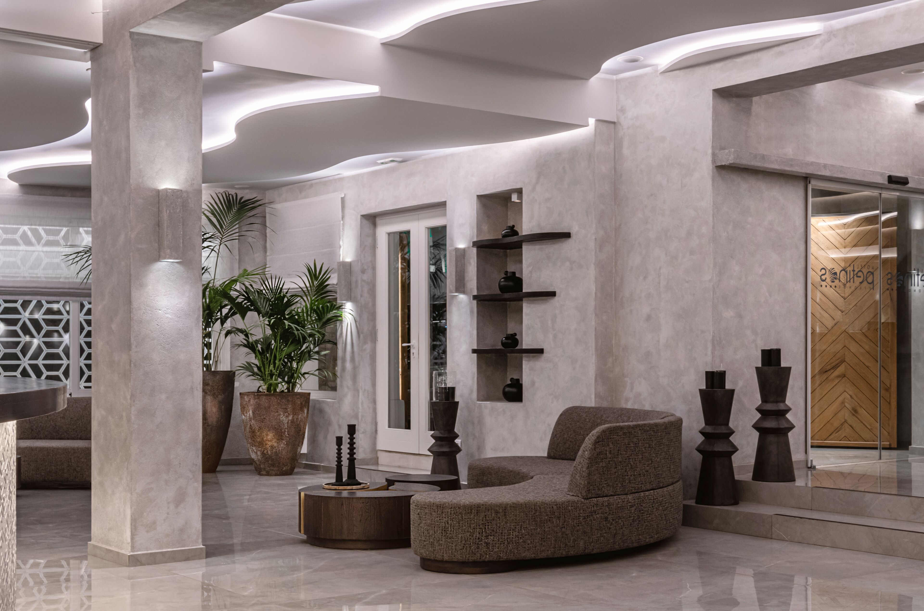 Een moderne lobby met een gebogen bank, grote potplanten en een houten deur.