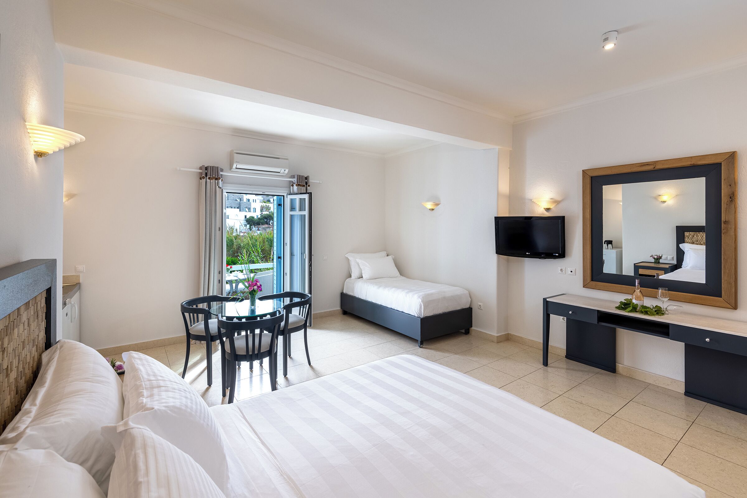 A hotel room with a bed, a desk, a chair, a TV, and a large window with curtains.