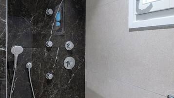 Ein modernes Badezimmer mit schwarzem Marmor an der Duschwand, einer Handbrause, einem wandmontierten Wasserhahn und einem kleinen Fenster über dem Spiegel.