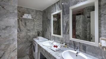 Un baño moderno con paredes de mármol, dos lavamanos, un espejo y lavadora integrada.