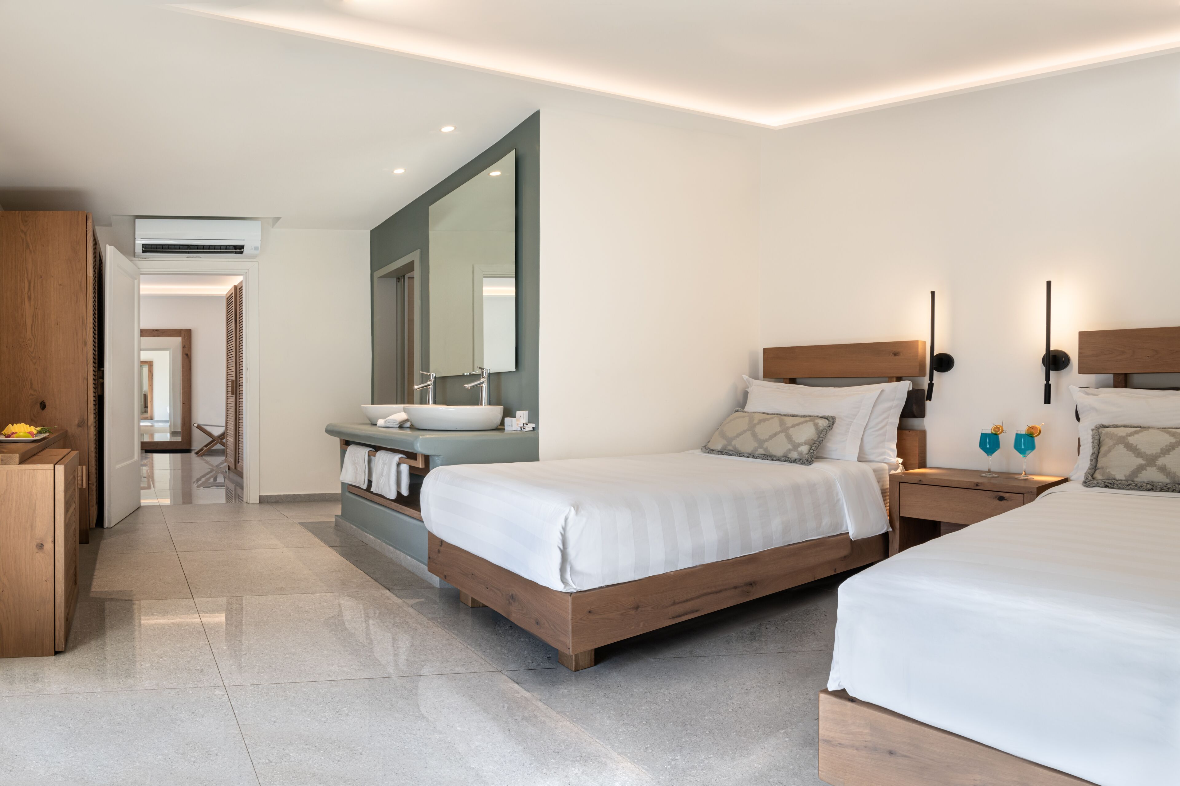 Una habitación de hotel moderna con dos camas, un espejo grande, un tocador con lavabo y un armario de madera.