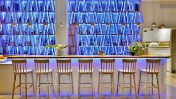 A bar area with a modern design, featuring a wall of illuminated shelves displaying bottles and a bar counter with wooden stools.