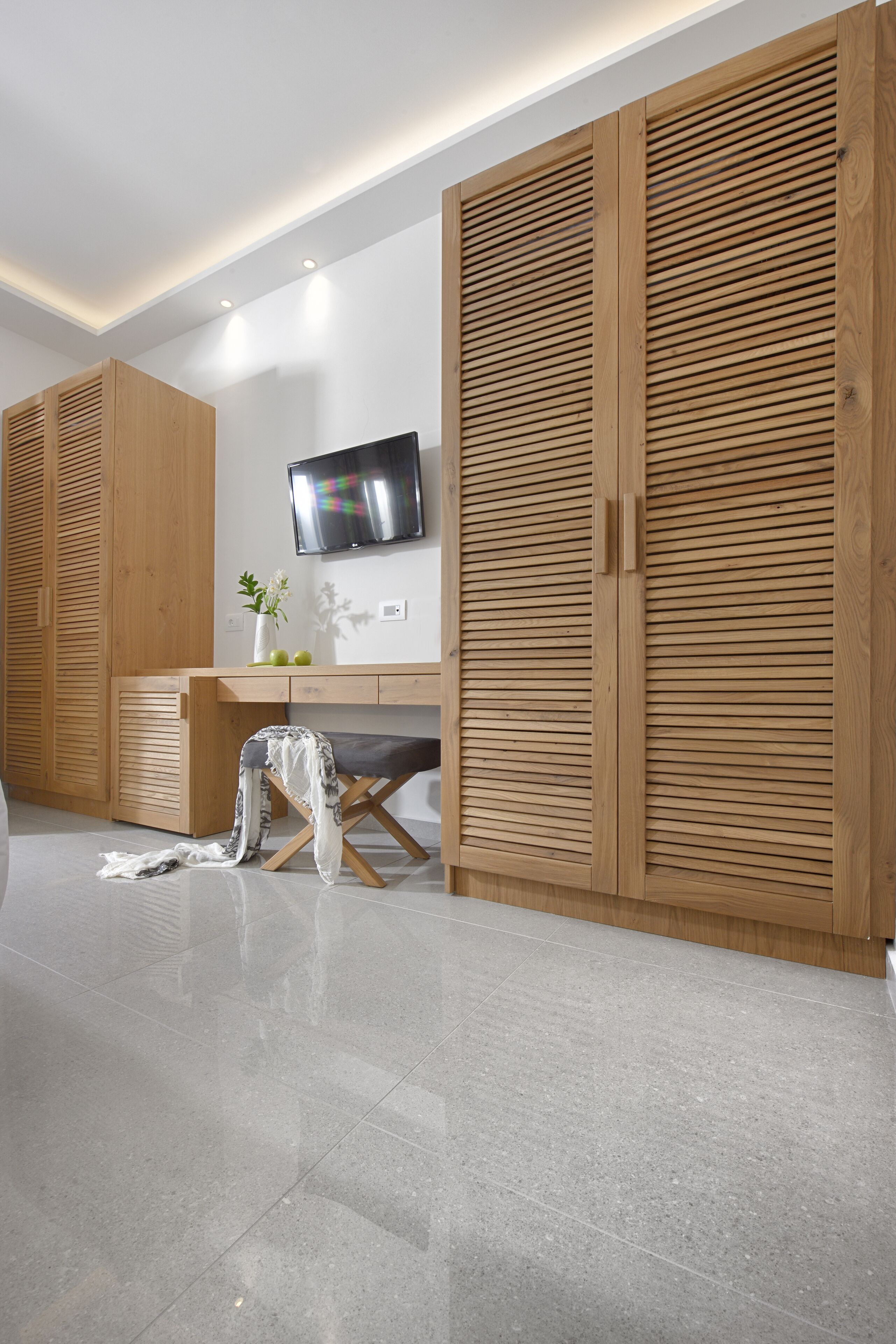 A modern room with wooden cabinets, a flat-screen TV, and a desk with a vase and plant.