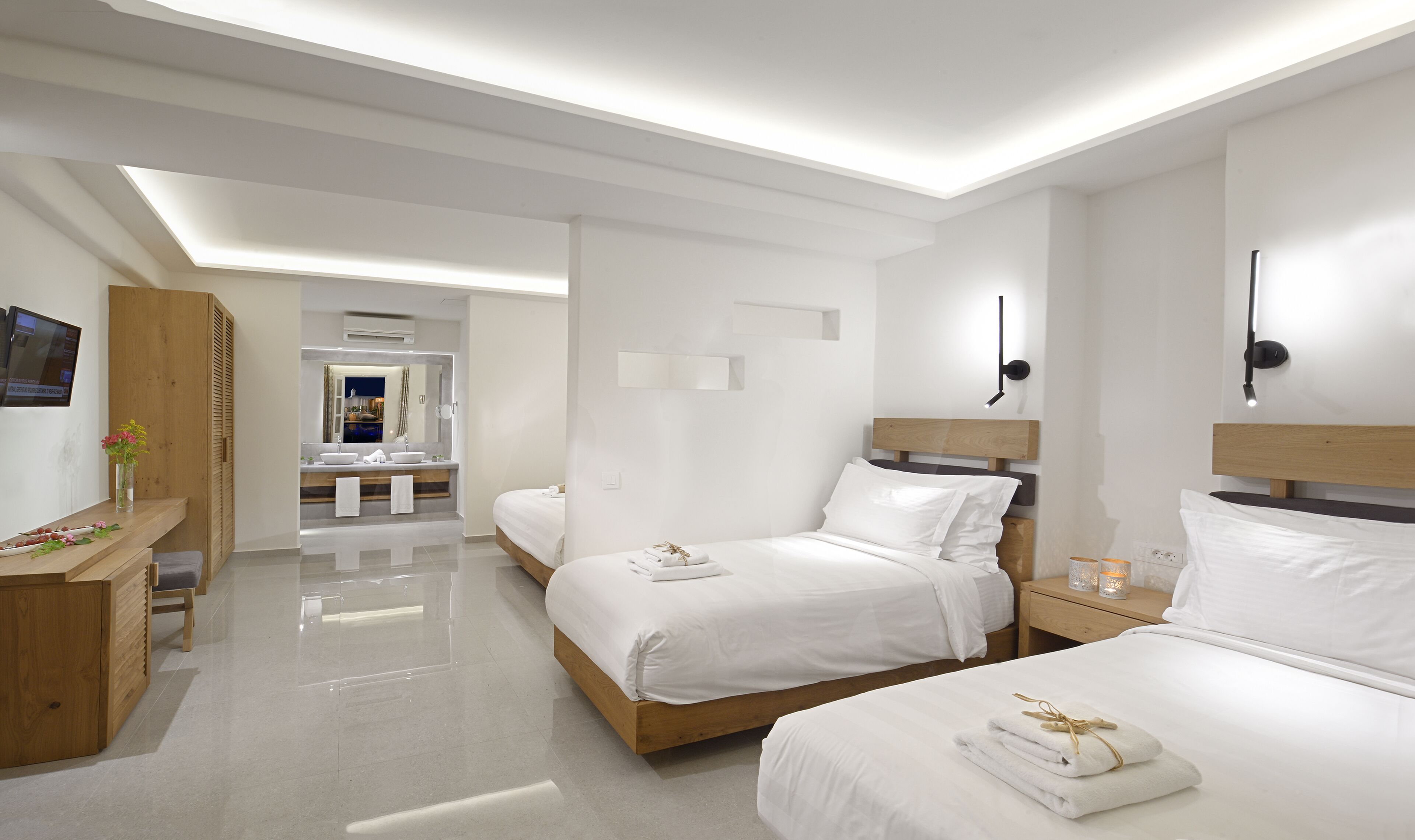 Habitación de hotel moderna con dos camas, un tocador con espejo, un escritorio y un baño visible a través de una puerta abierta.