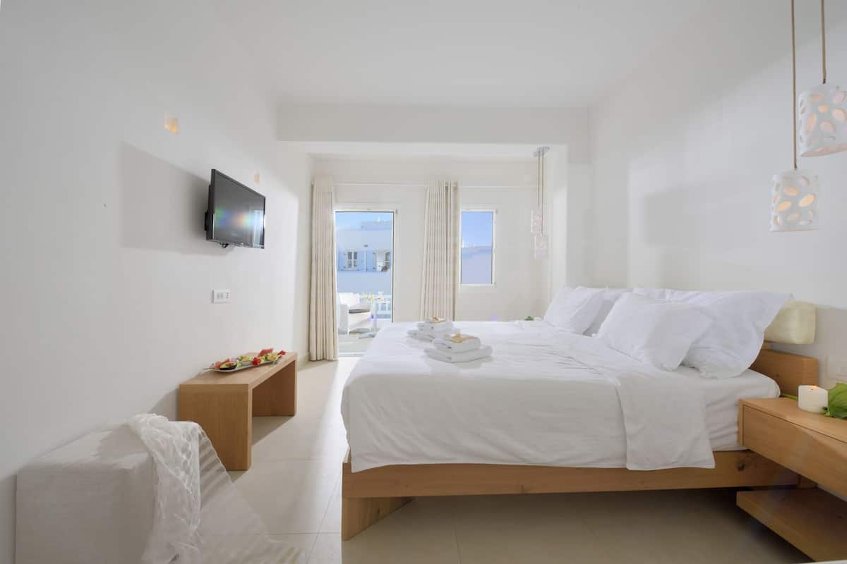 A modern hotel room with a large bed, a TV mounted on the wall, a bedside table with a lamp, and a view of the city through the window.