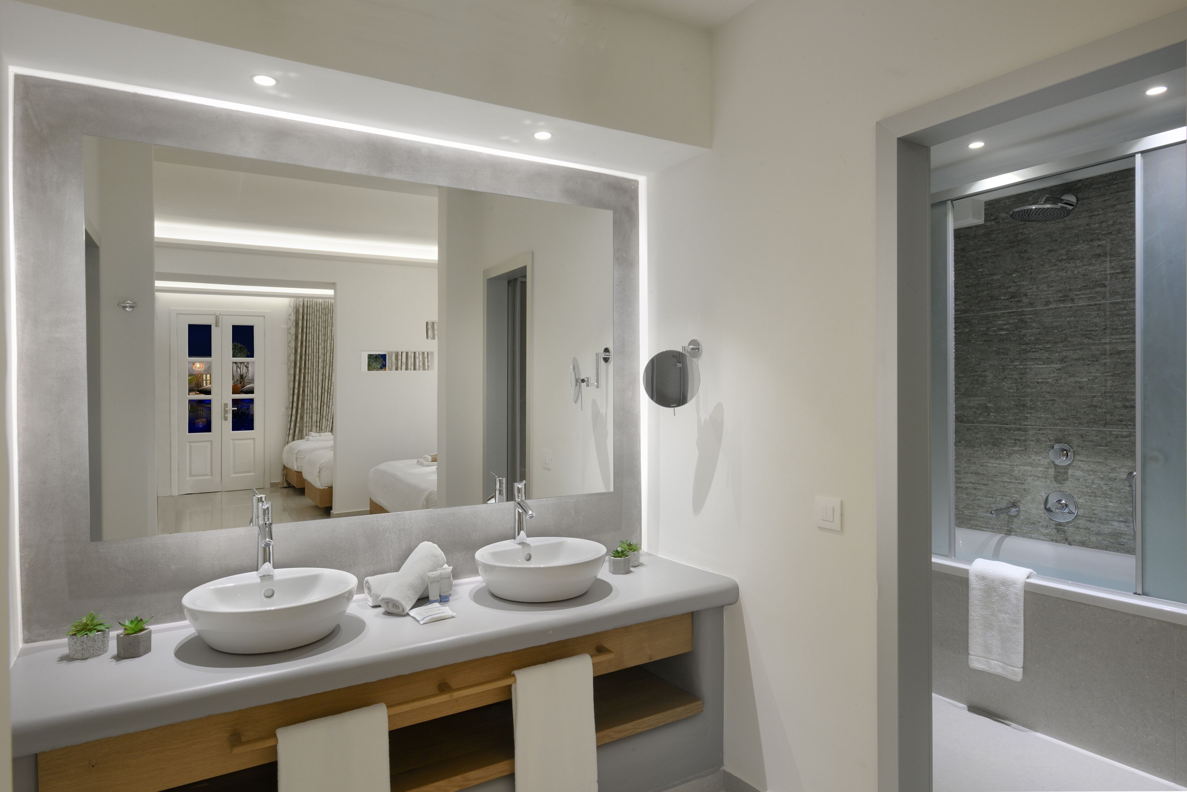 A modern bathroom with two sinks, a large mirror, and a shower area.