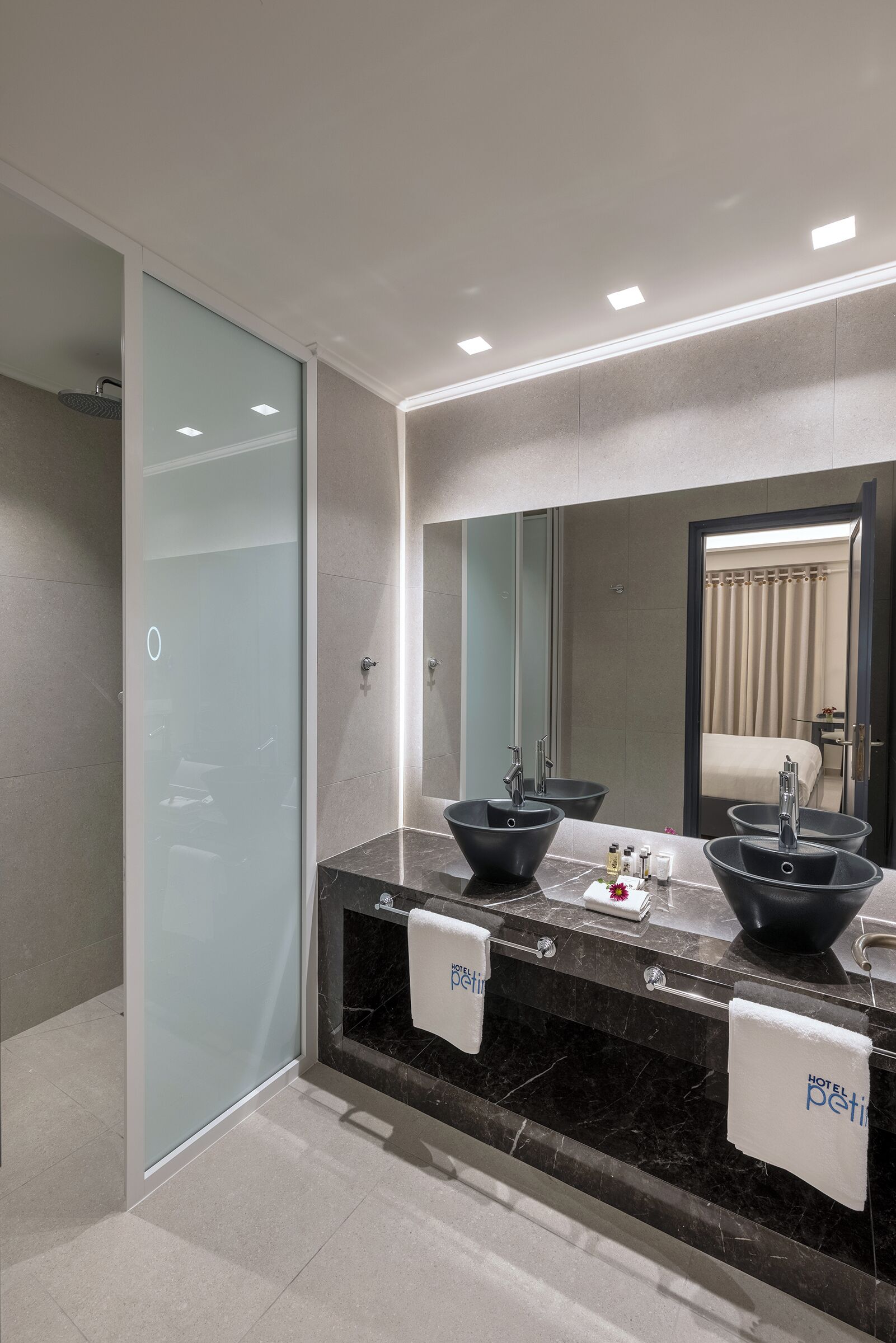 A modern bathroom with a large mirror, two black vessel sinks, and a glass shower enclosure.