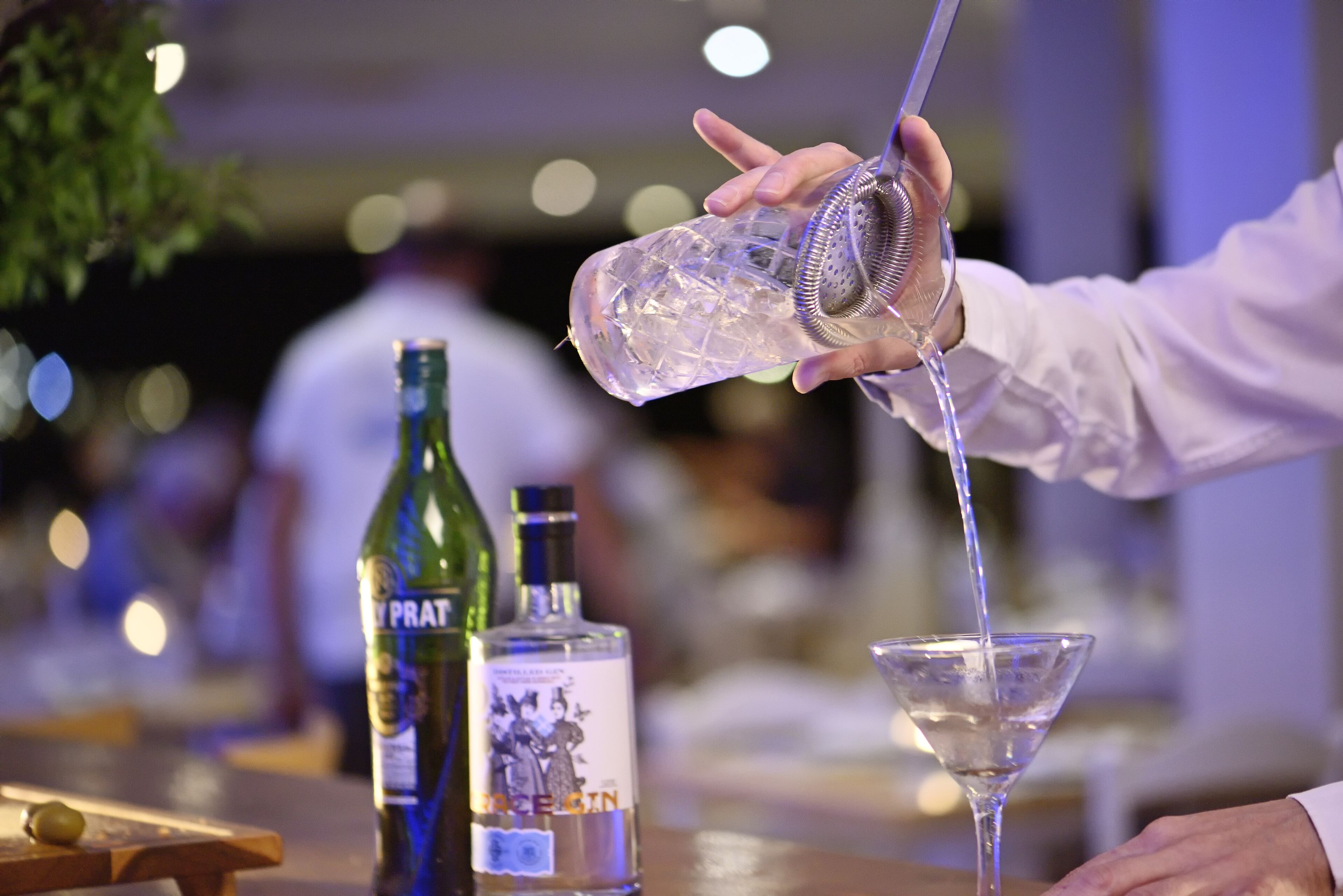 A bartender pouring a drink into a martini glass.