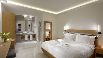 Una habitación de hotel moderna con una cama grande, mesitas de noche, un cabecero de madera, un tocador con espejo y un baño visible a través de una puerta abierta.