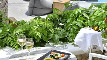 Zona de comedor junto a la piscina, con una mesa para dos, una botella de vino y un plato de comida.