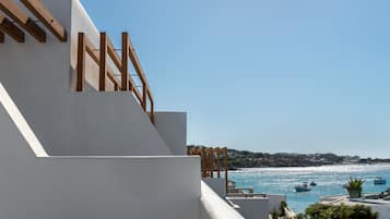 A coastal building with a balcony overlooking the sea, wooden railings, and a clear view of boats.