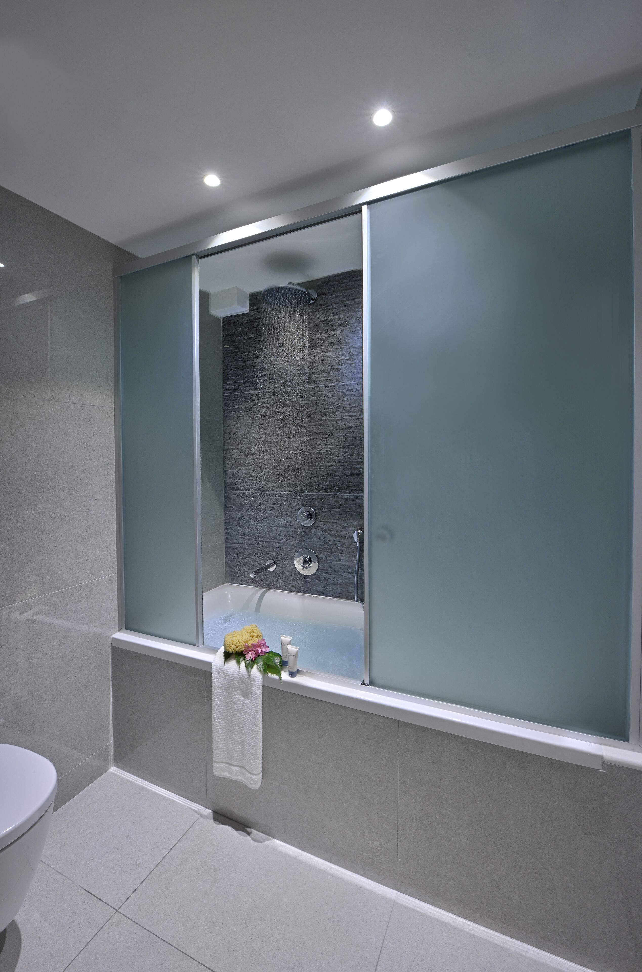 A modern bathroom with a glass-enclosed shower, a white toilet, and a towel rack with a floral arrangement.