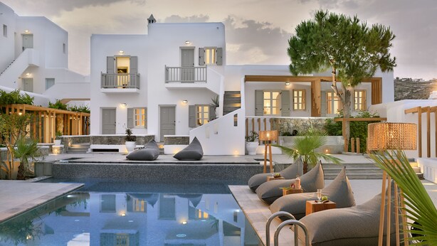 A pool area with a clear view of the pool, a set of lounge chairs, and a staircase leading to a building with balconies. - Hotel Petinos (Mykonos)