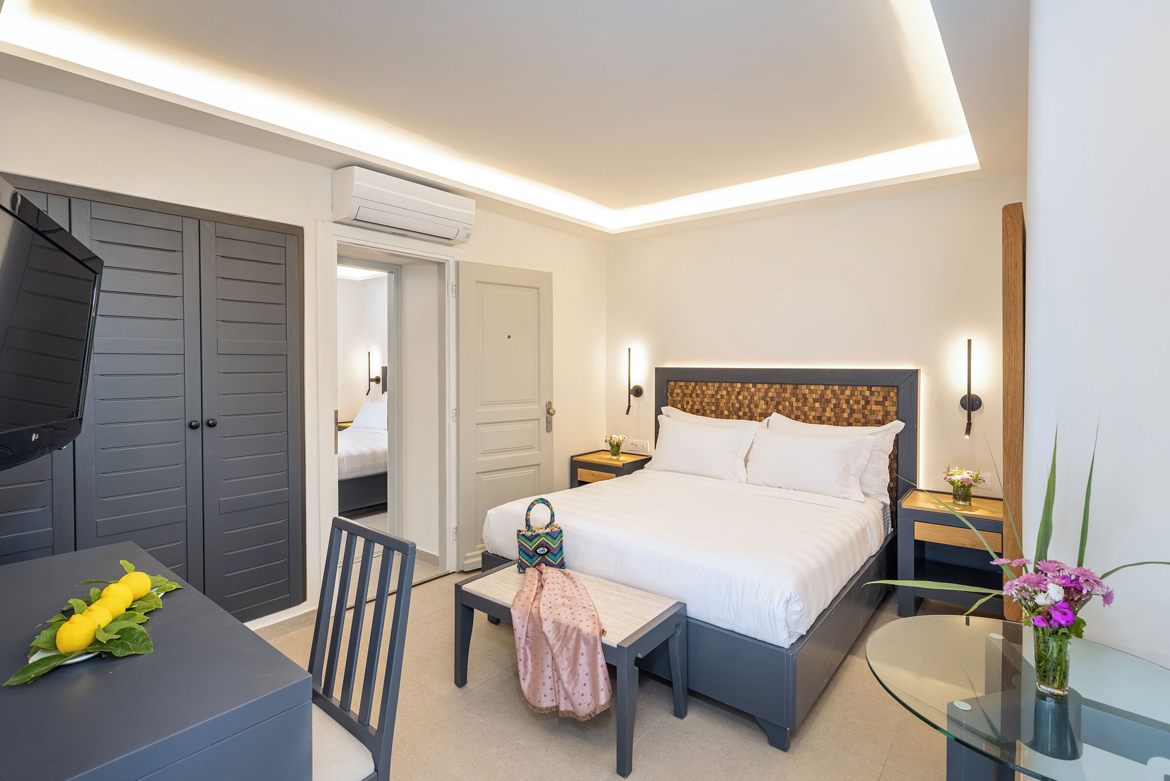 A modern hotel room with a bed, bedside table, chair, and a desk with a chair.