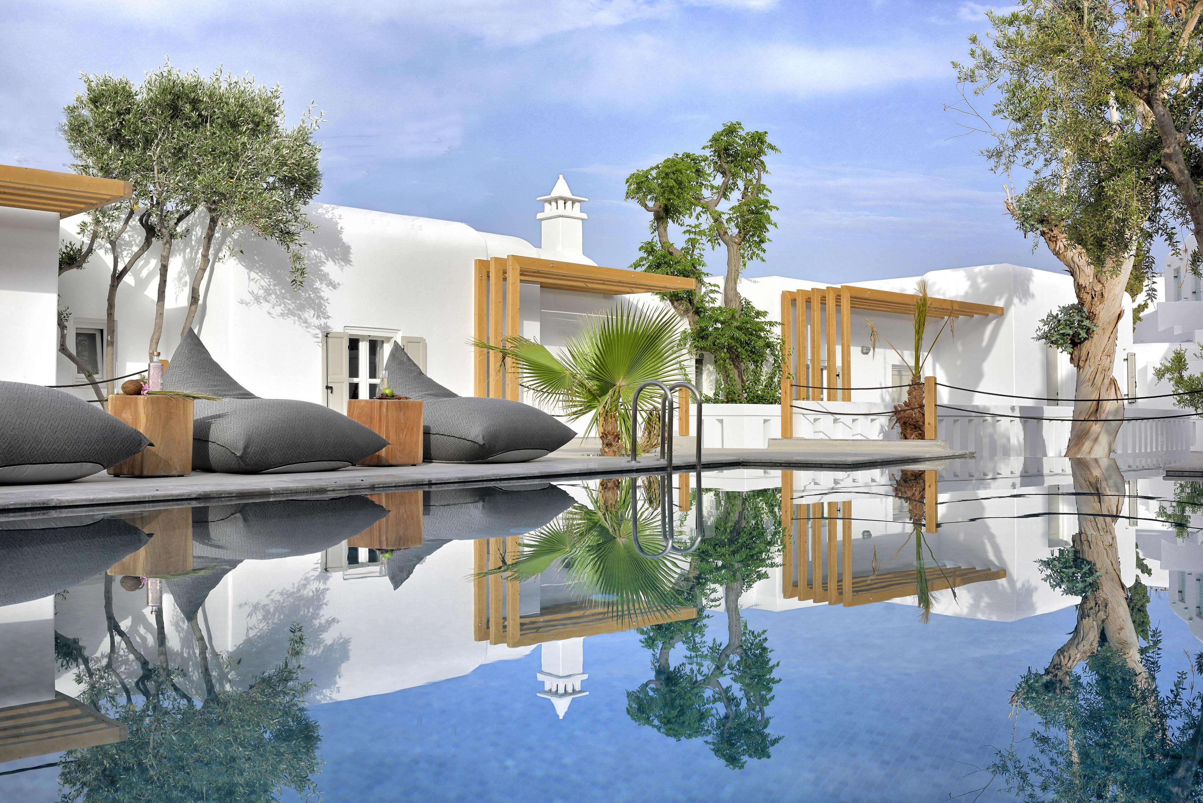 Un área de piscina tranquila con edificios blancos, pérgolas de madera y abundante vegetación.