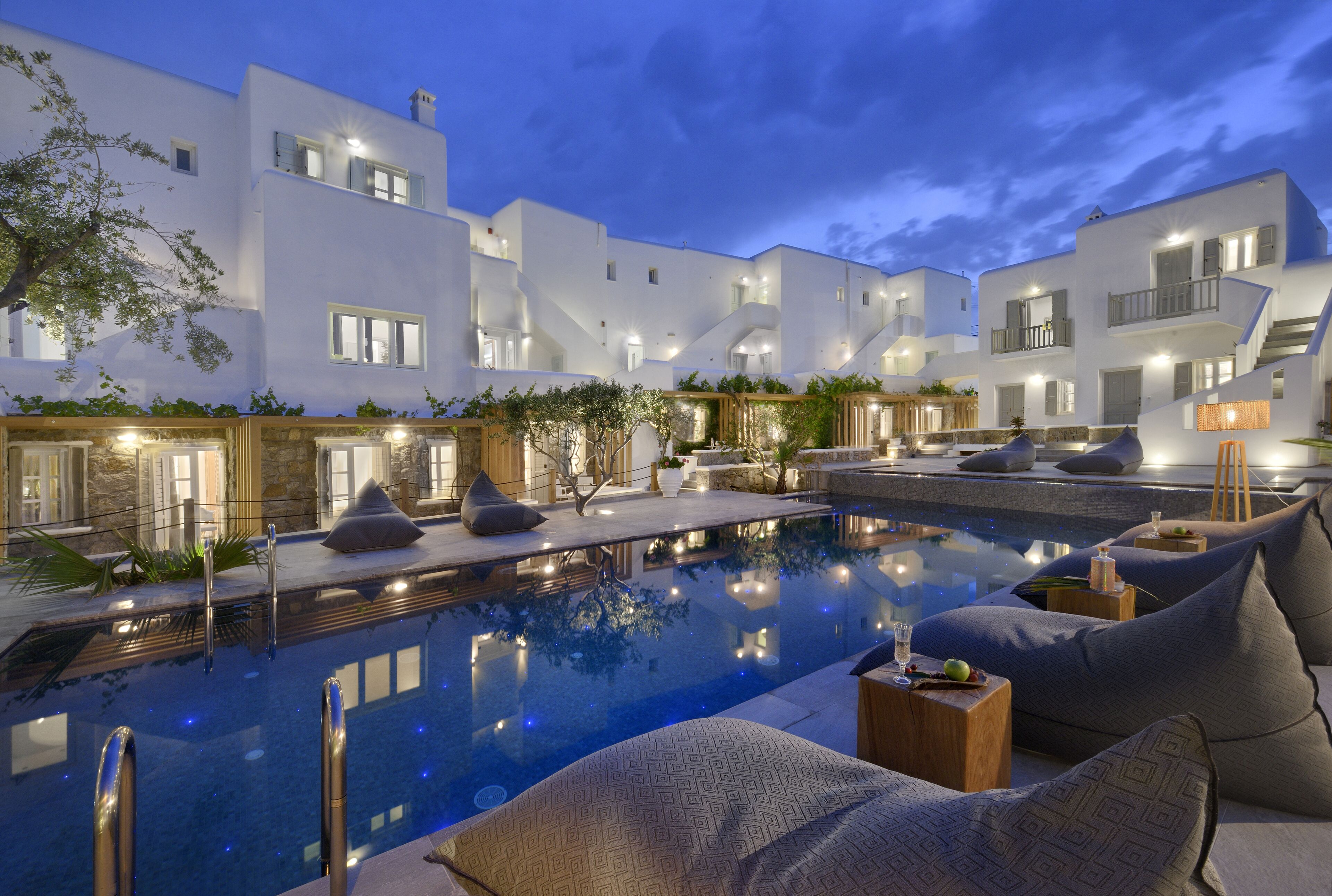 A modern pool area with a clear view of the pool, lounge chairs, and a white building with balconies.