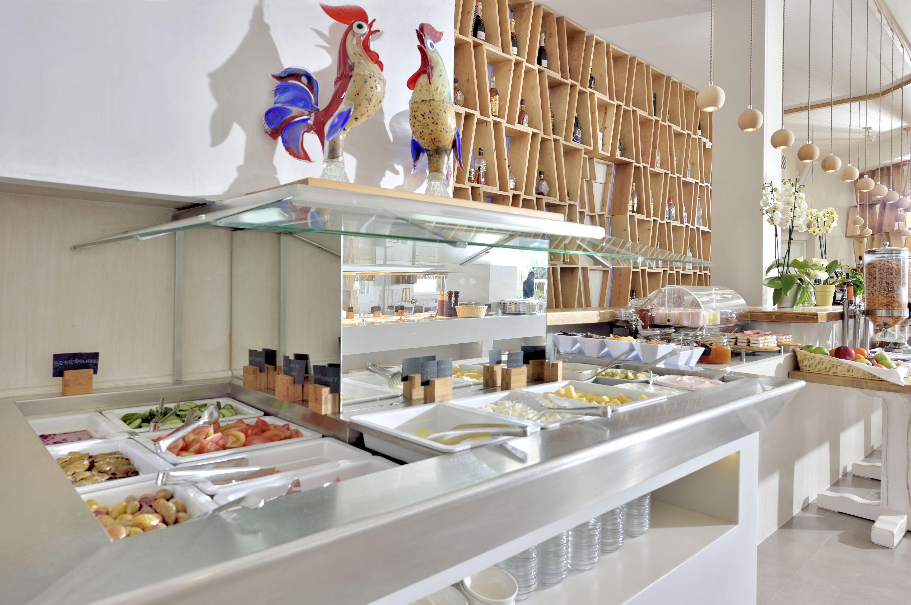 Un buffet proposant une variété de plats, une étagère en bois avec des bouteilles et des sculptures décoratives représentant des coqs.