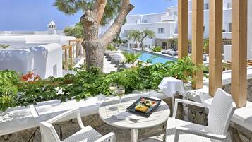 Une terrasse avec des meubles blancs, une table dressée pour le repas, et une vue sur une piscine et des bâtiments blancs.