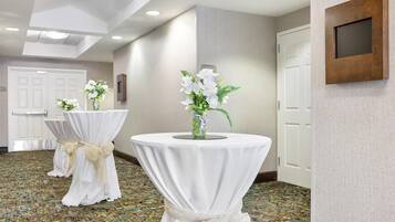 A hallway with round tables covered in white tablecloths and tied with beige sashes, a wall-mounted TV, and a patterned floor.