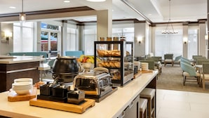 Un espace dédié au petit-déjeuner dans l’hôtel, avec un buffet proposant notamment un coin café, un assortiment de fruits et une variété de pains.