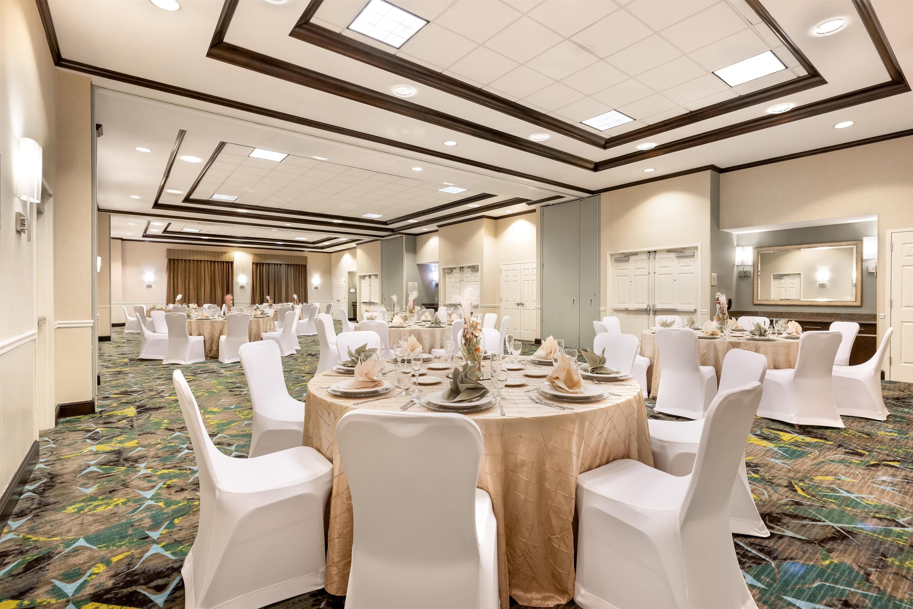 A banquet hall with round tables set for a formal event, featuring white chairs and table settings.
