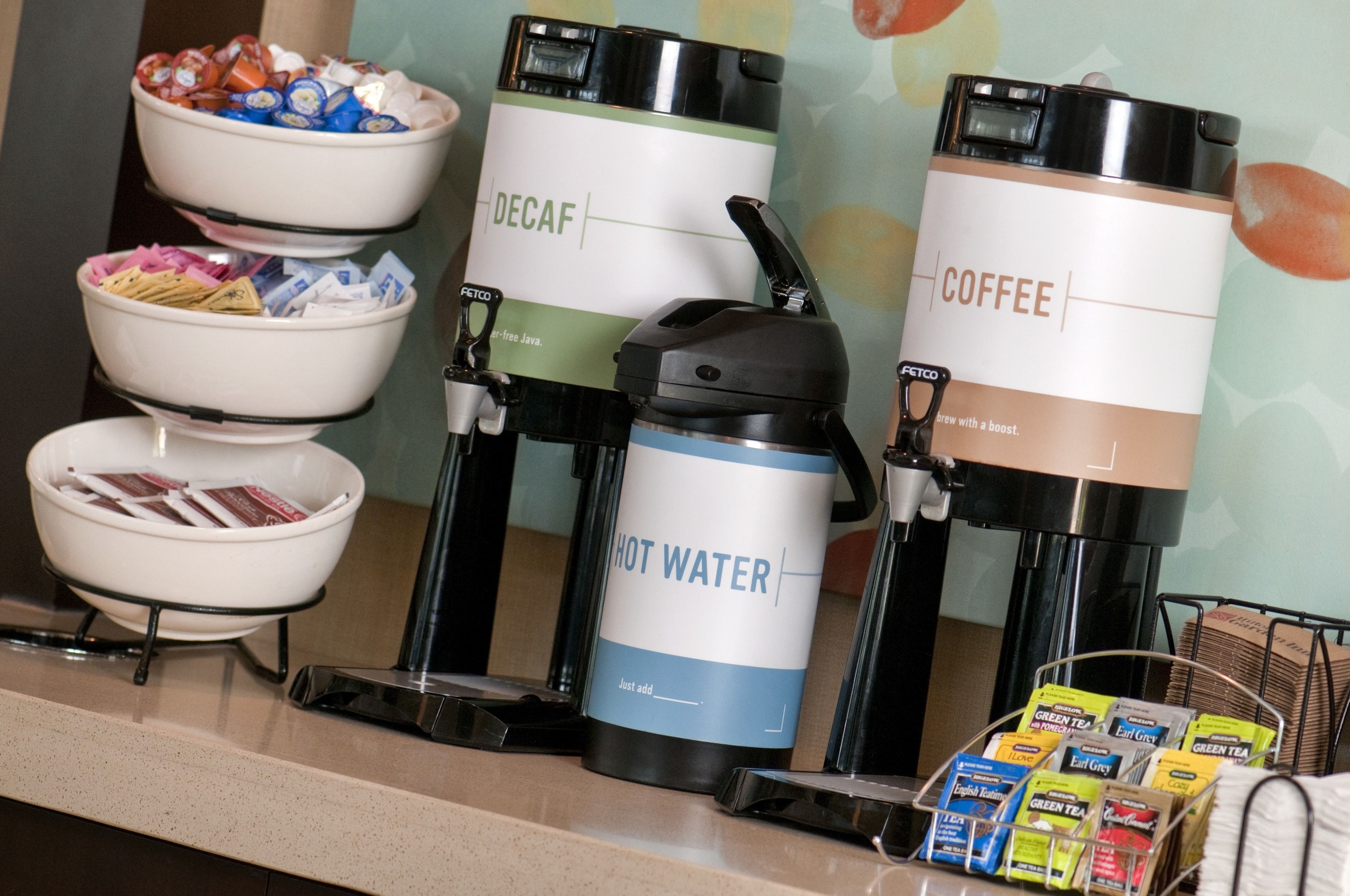 Eine Kaffeestation mit Automaten für entkoffeinierten Kaffee, Kaffee und heißes Wasser, sowie eine Schüssel mit Snacks.