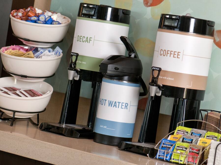 Eine Kaffeestation mit Automaten für entkoffeinierten Kaffee, Kaffee und heißes Wasser, sowie eine Schüssel mit Snacks.