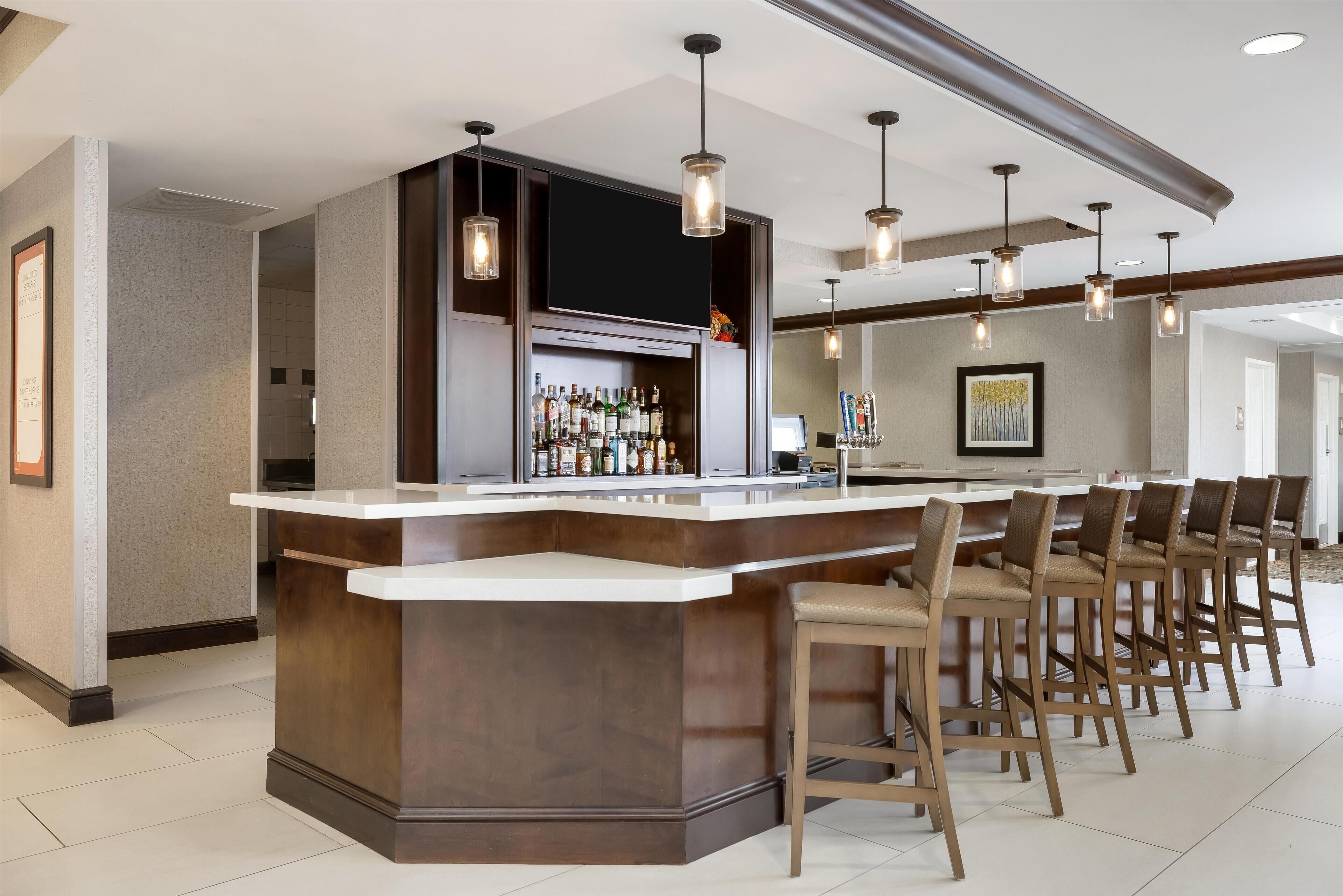 A bar area with a counter, stools, and hanging pendant lights.
