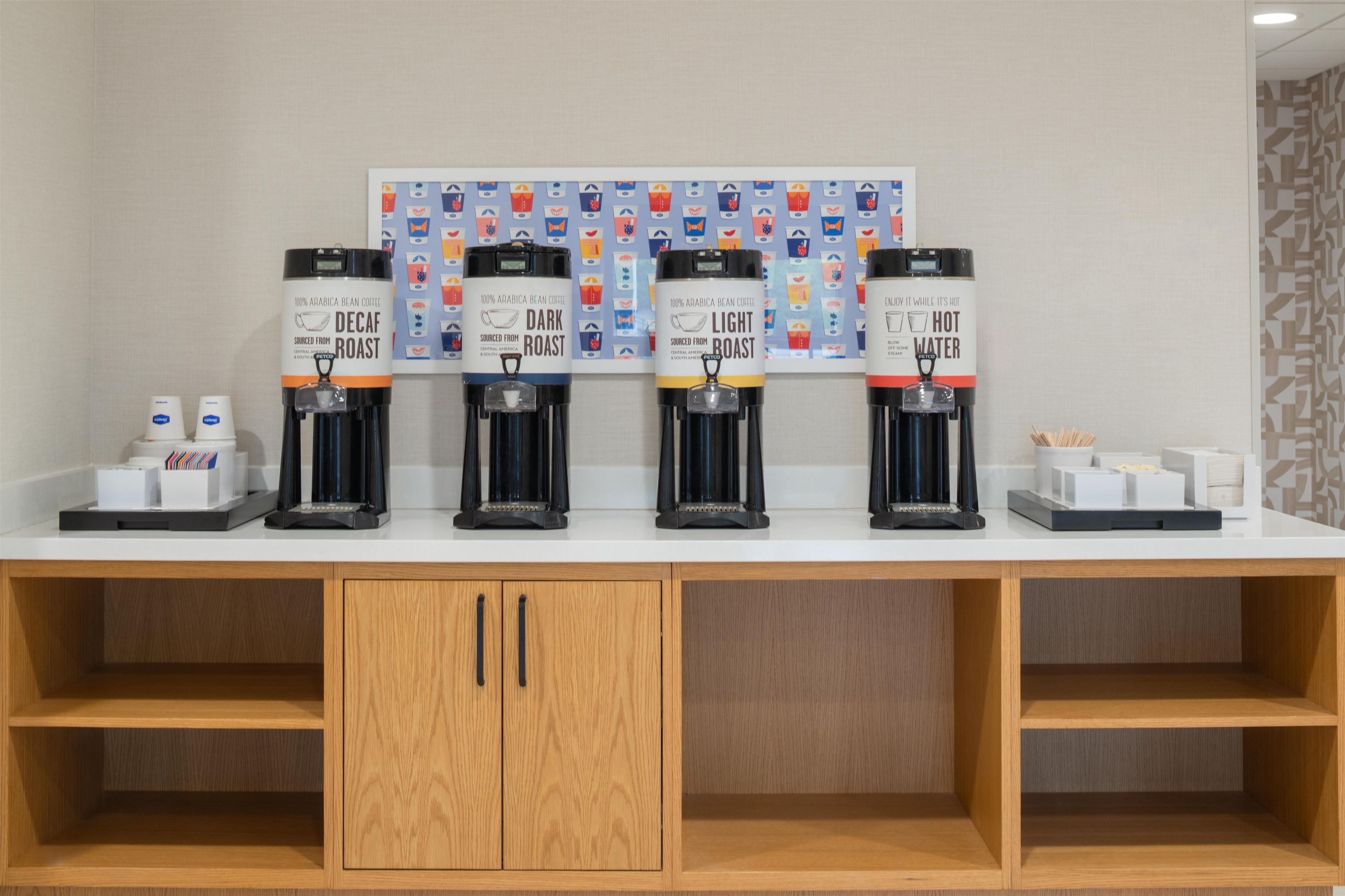 A coffee station with four dispensers labeled 'Decaf,' 'Dark Roast,' 'Light Roast,' and 'Hot Water.'