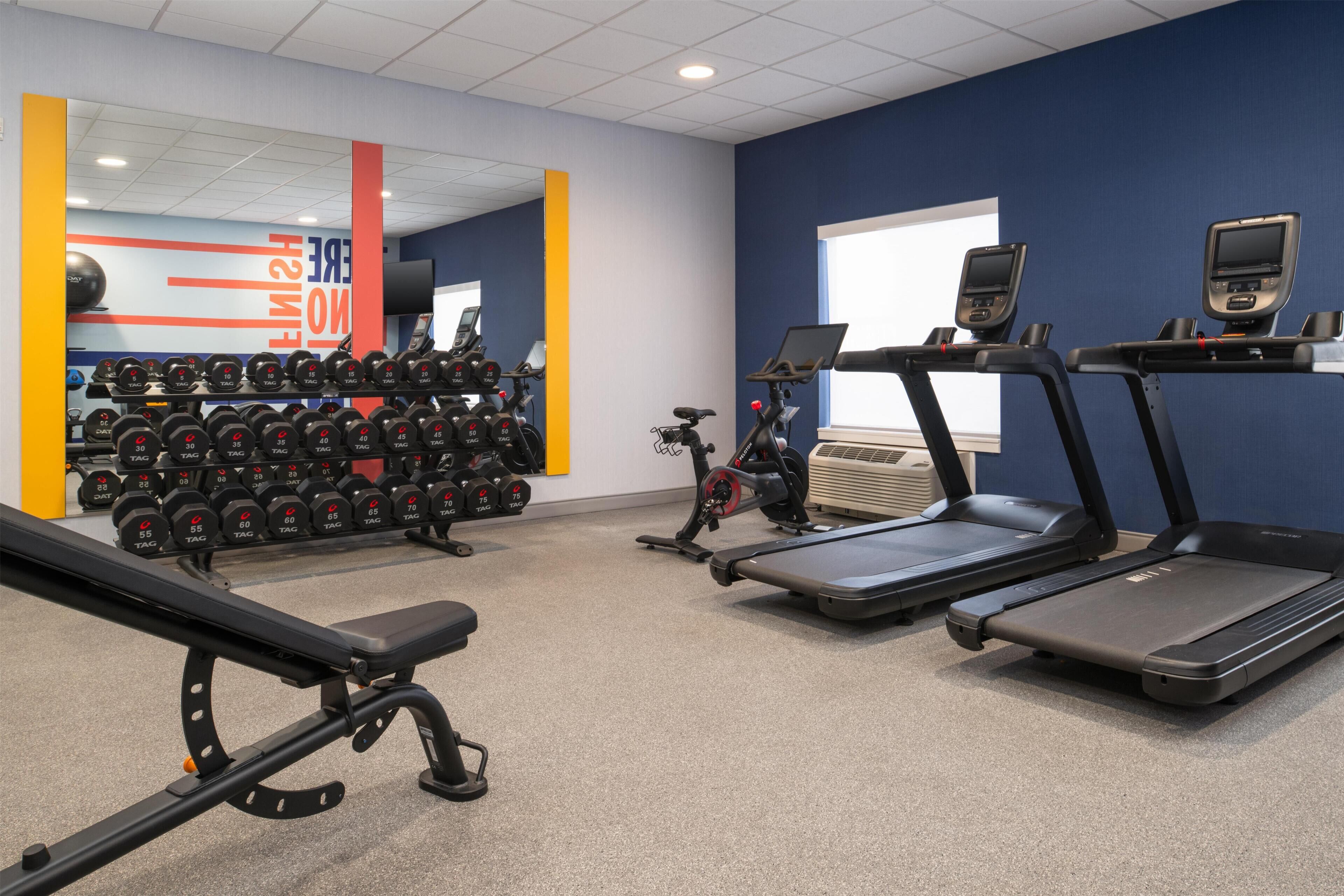 Une salle de sport équipée de tapis de course, d’haltères et d’un banc de musculation.