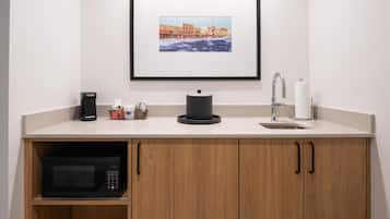 Una kitchenette equipada con microondas, cafetera, hervidor de agua y un cuadro enmarcado en la pared.