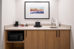Una kitchenette equipada con microondas, cafetera, hervidor de agua y un cuadro enmarcado en la pared.