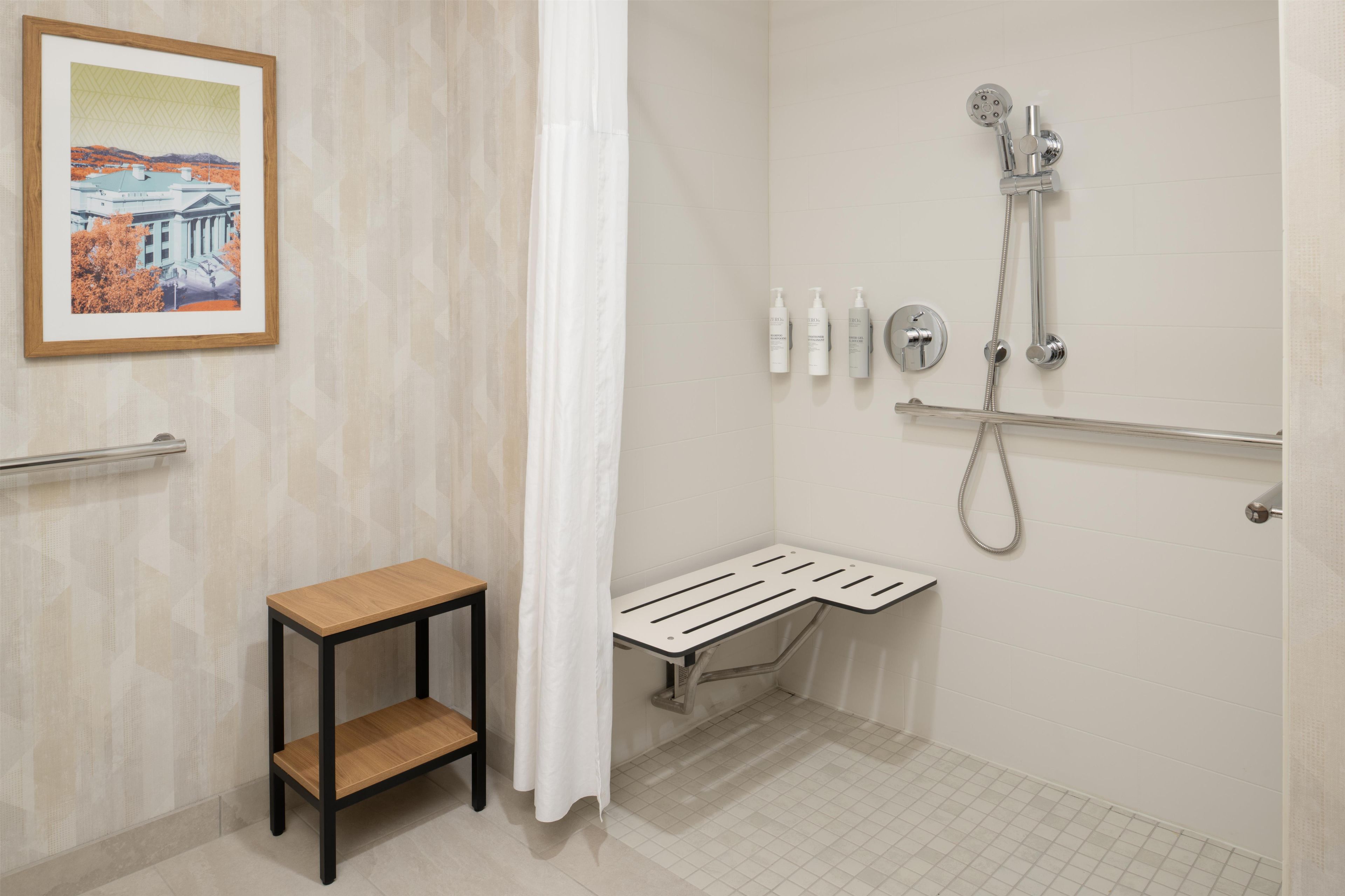 A bathroom with a shower, a small table, a framed picture on the wall, and a handrail.