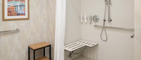 A bathroom with a shower, a small table, a framed picture on the wall, and a handrail.
