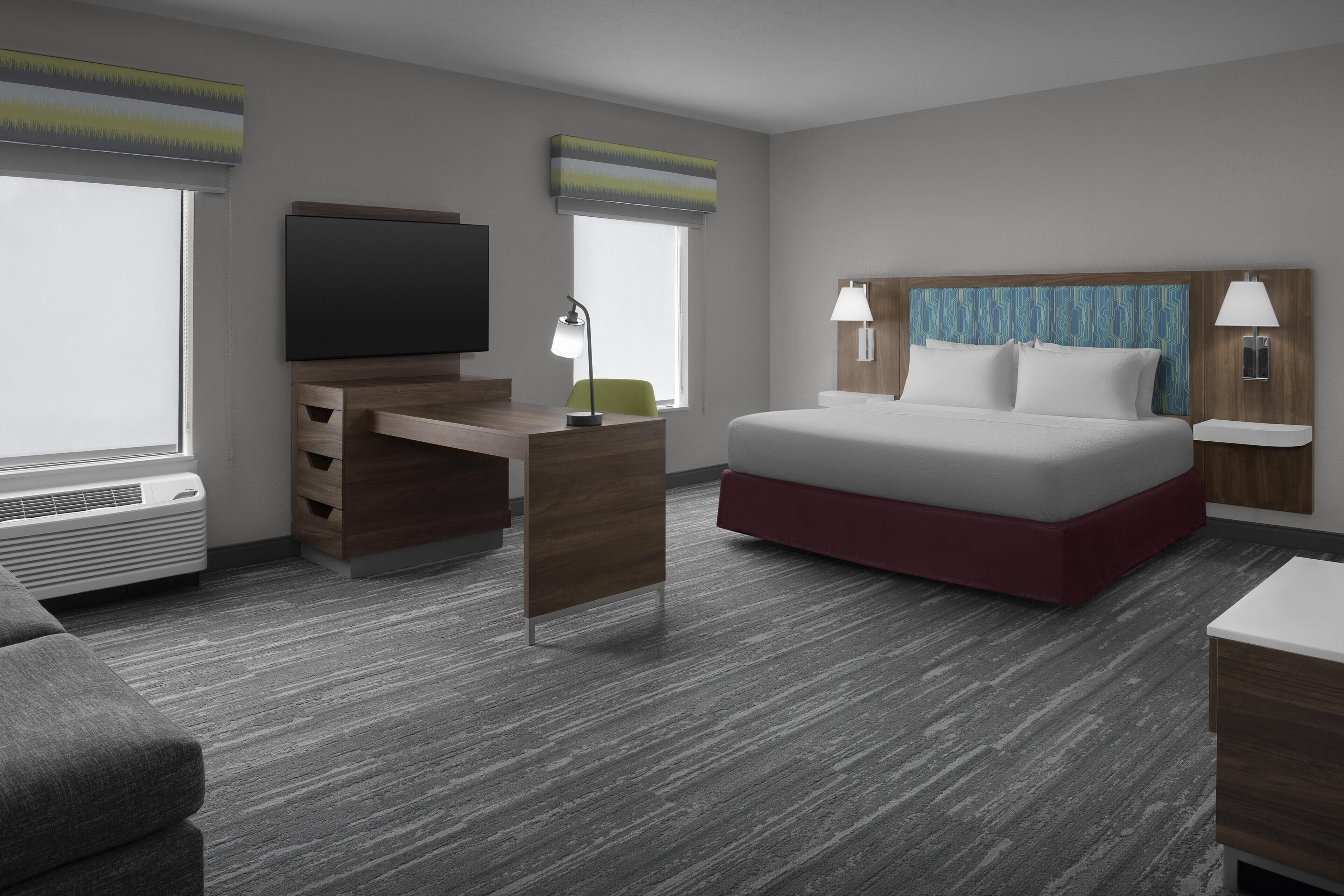 A modern hotel room with a bed, a desk, a television, and a window.