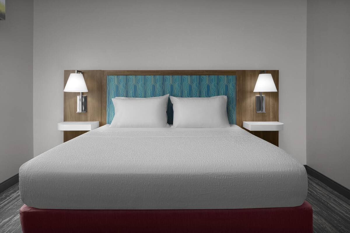 A hotel room with a large bed, two bedside lamps, and a patterned headboard.