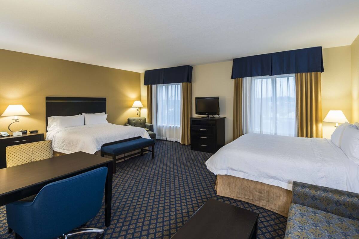 A hotel room with two beds, a desk, a chair, a TV, and a minibar.