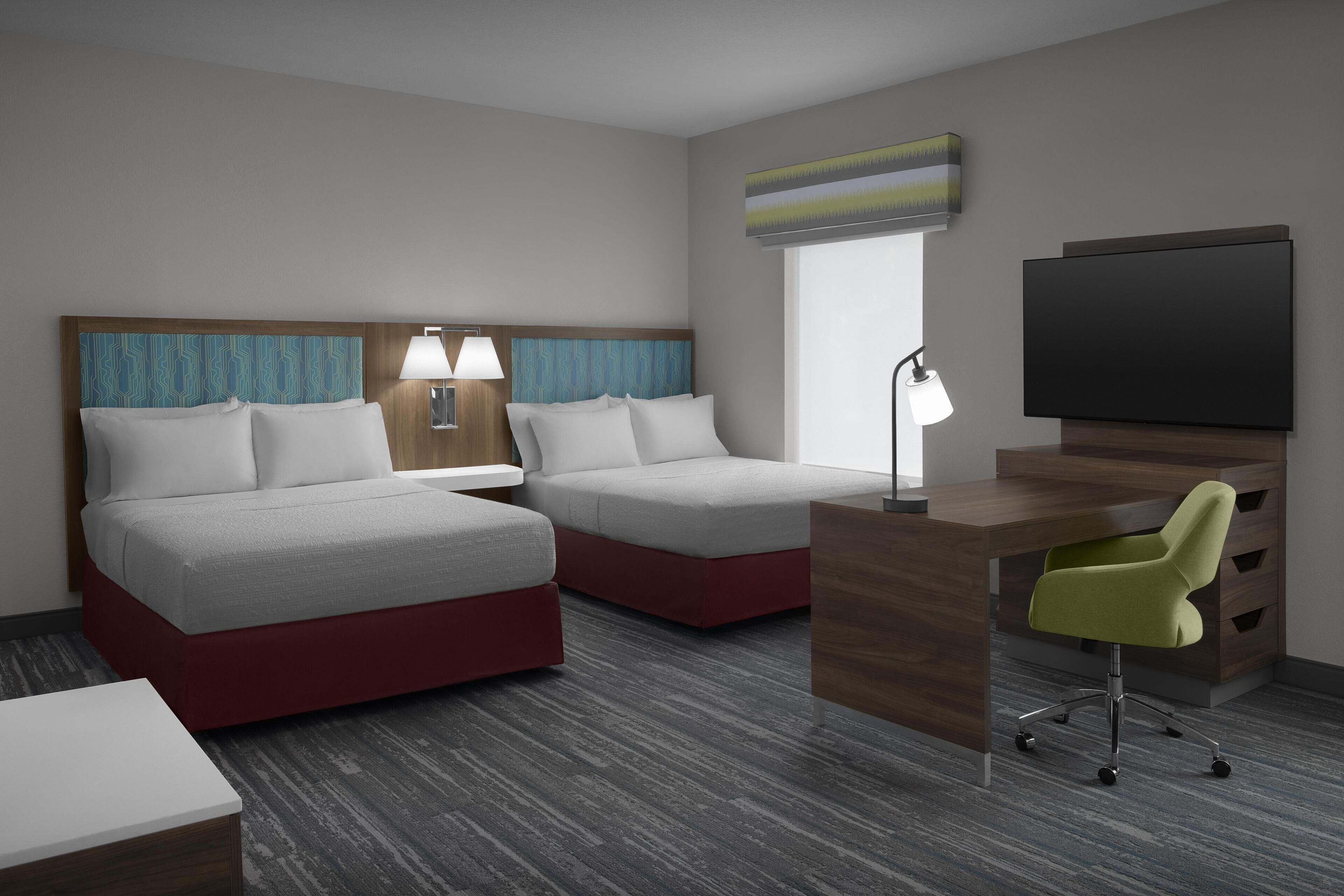 Une chambre d’hôtel avec deux lits, un bureau, une chaise, une télévision et une fenêtre.