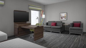 Una habitación de hotel moderna con televisor de pantalla plana, un escritorio de madera, un sofá gris con cojines rojos, dos sillones, una pequeña mesita auxiliar y un cuadro en la pared.